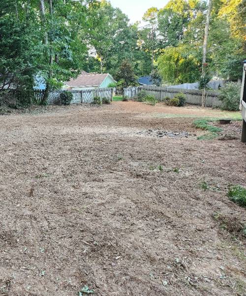 A yard with a fence and trees in the background